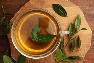 Photo of Cup of freshly brewed tea with bay leaves on wooden table, flat lay