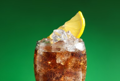 Photo of Glass of refreshing soda drink with ice cubes and lemon on green background, closeup