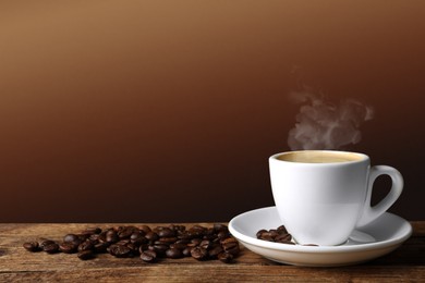 Cup of hot aromatic coffee and roasted beans on wooden table against brown background. Space for text