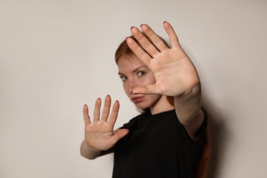 Photo of Young woman making stop gesture against light background, focus on hand