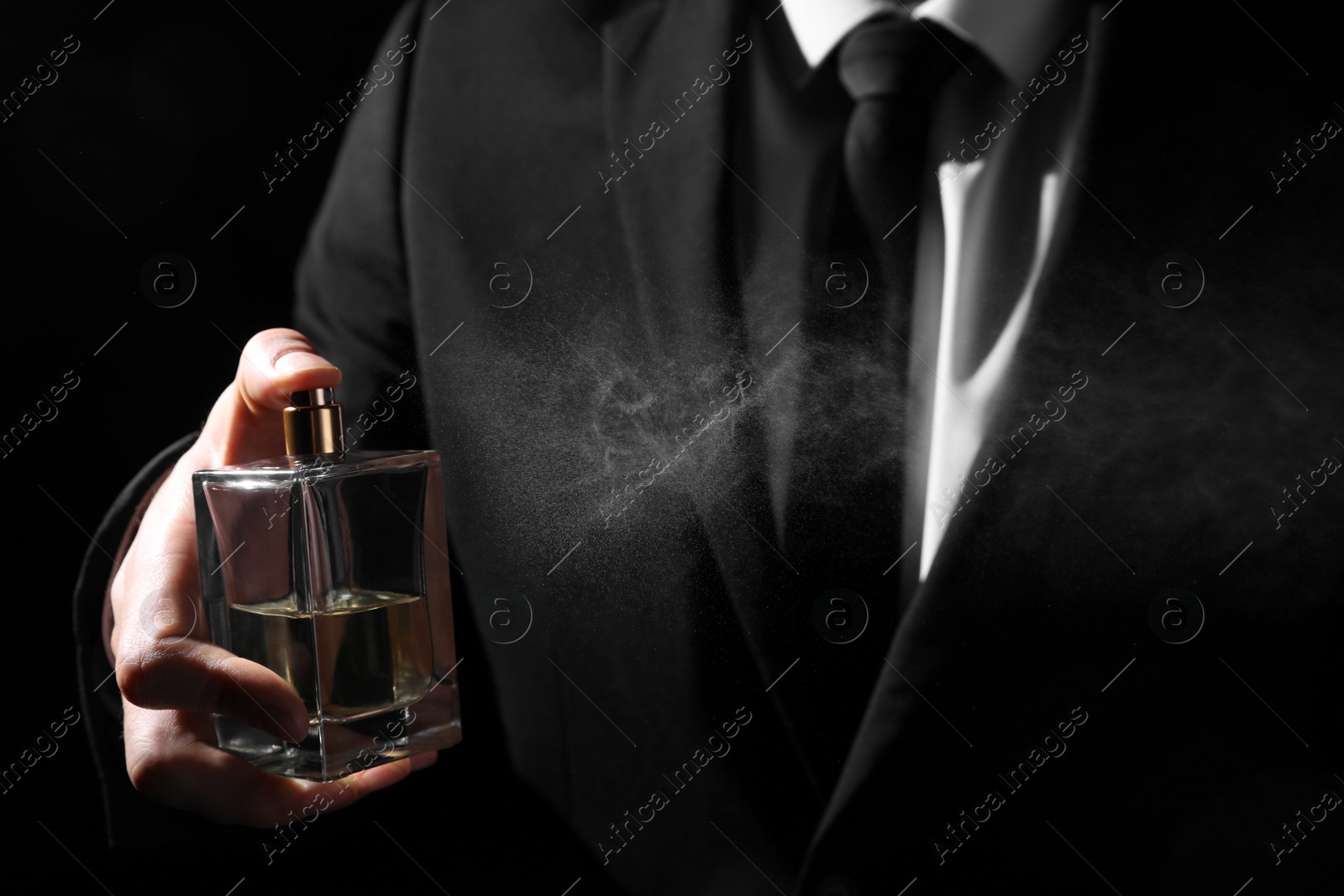 Photo of Man spraying luxury perfume on black background, closeup