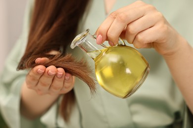 Photo of Woman applying oil hair mask onto ends at home, closeup