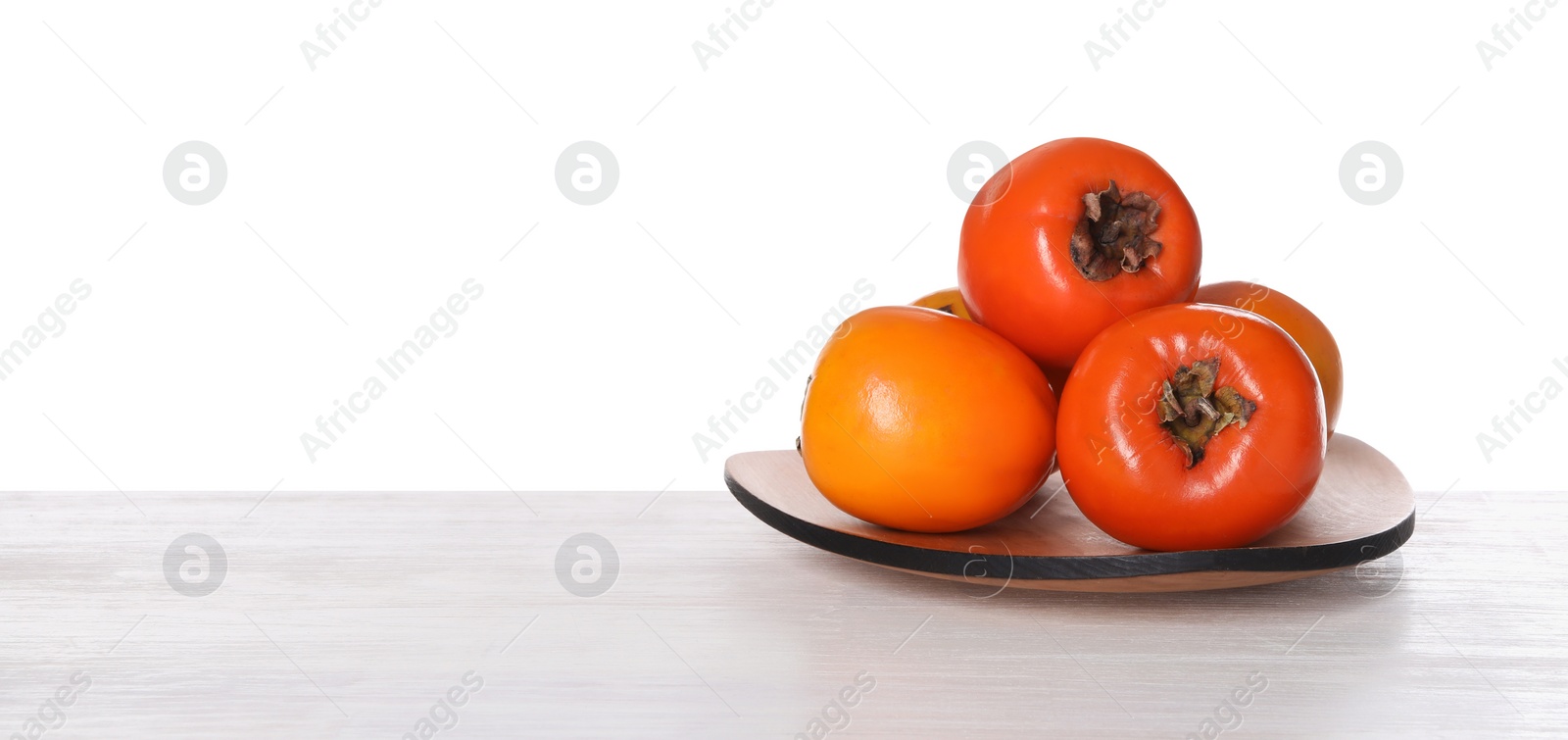 Photo of Delicious ripe juicy persimmons in plate on wooden table against white background