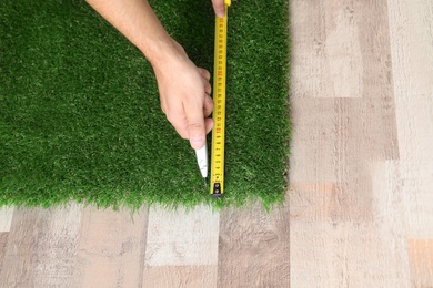 Man cutting artificial grass carpet indoors, top view. Space for text