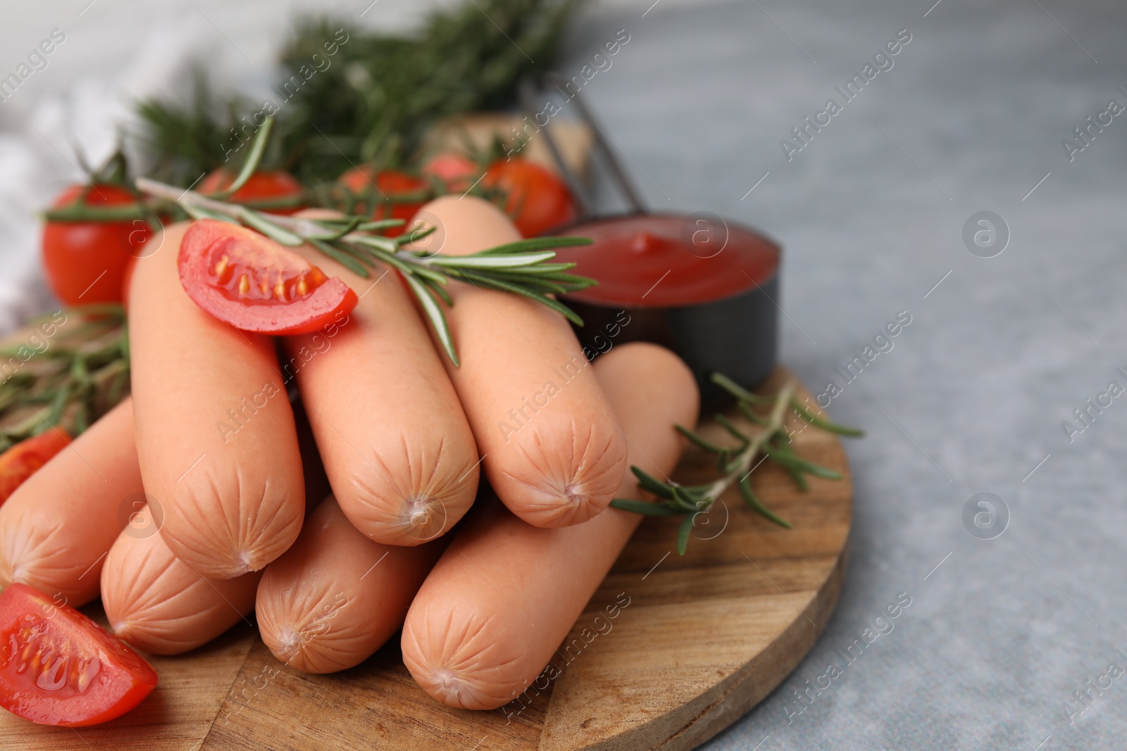 Photo of Delicious boiled sausages, tomatoes and rosemary on gray table, closeup