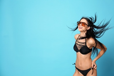 Photo of Beautiful young woman in stylish bikini with sunglasses on light blue background. Space for text