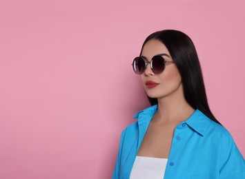 Photo of Attractive serious woman in fashionable sunglasses against pink background. Space for text