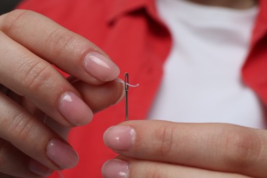 Photo of Woman inserting thread through eye of needle, closeup