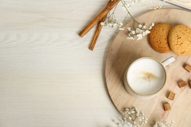 Cup of hot coffee, cookies, brown sugar and flowers on white wooden table, flat lay. Space for text