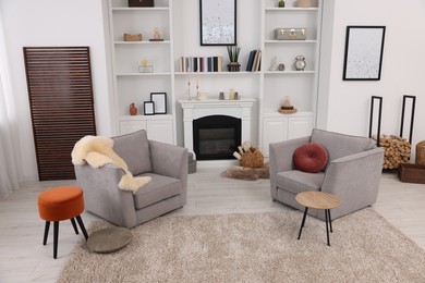 Comfortable armchairs, fireplace and shelves in living room. Interior design