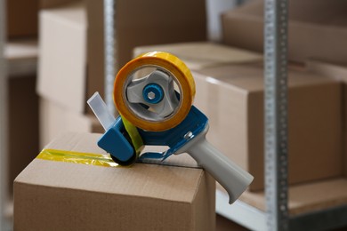 Photo of Taping cardboard box with adhesive tape dispenser indoors