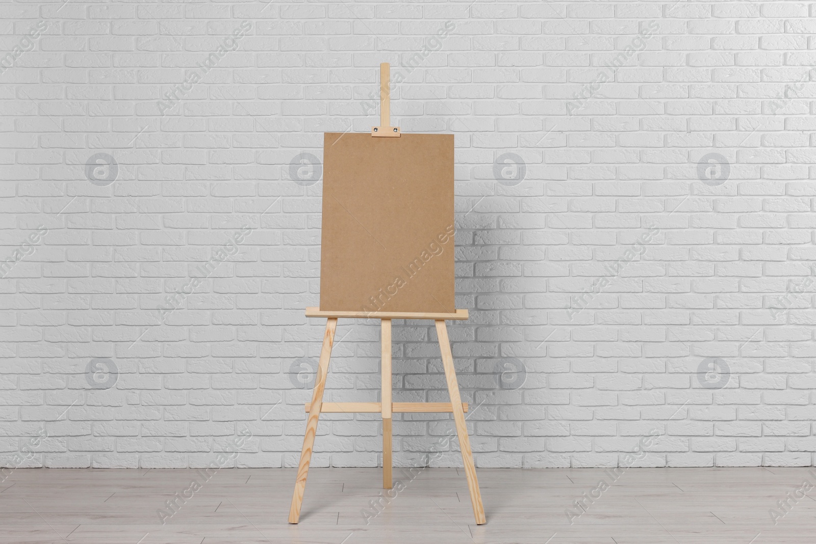 Photo of Wooden easel with blank board near white brick wall indoors
