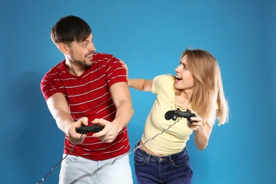 Emotional couple playing video games with controllers on color background