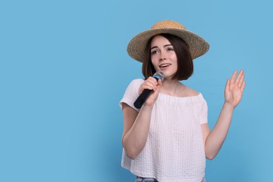 Beautiful woman in hat with microphone singing on light blue background, space for text