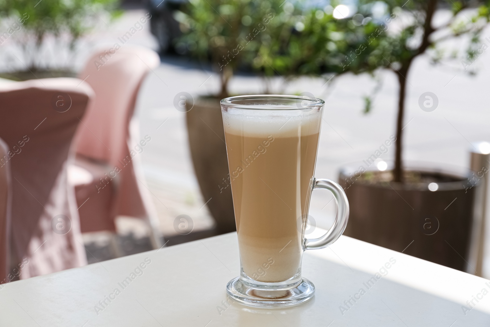 Photo of Glass with delicious coffee on white table in outdoor cafe
