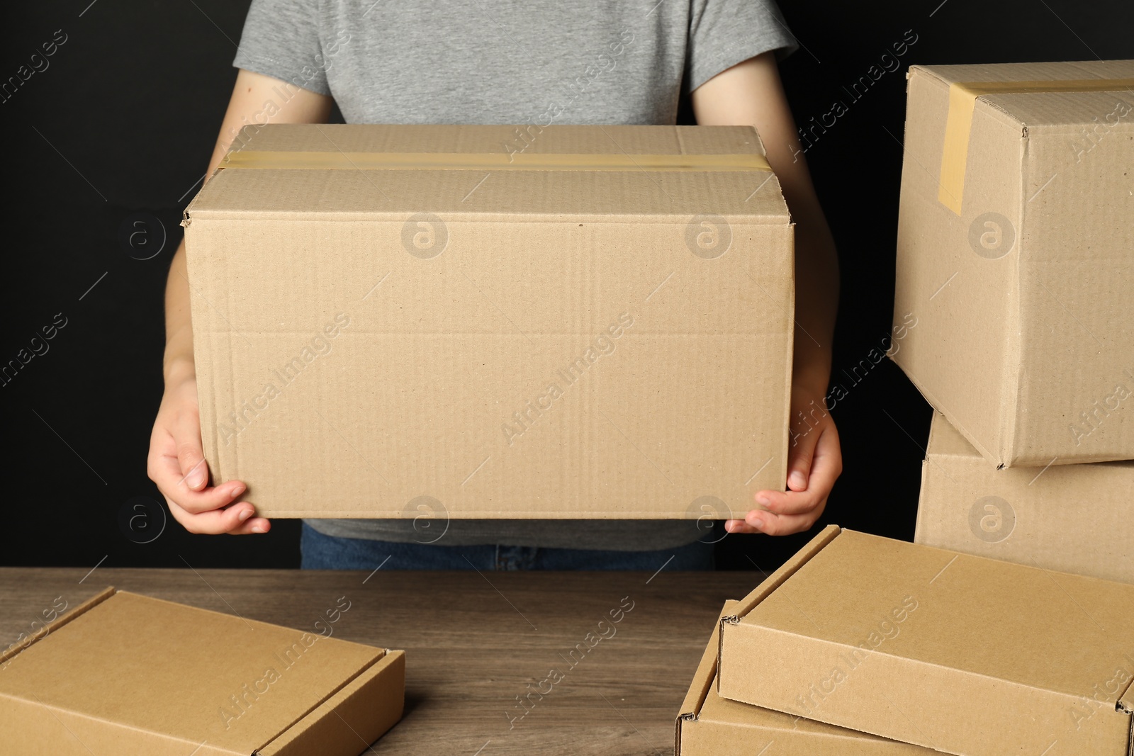 Photo of Packaging goods. Woman with cardboard boxes at wooden table, closeup