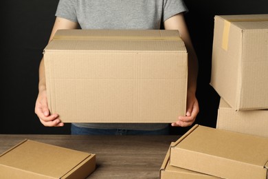 Packaging goods. Woman with cardboard boxes at wooden table, closeup