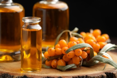 Photo of Natural sea buckthorn oil and fresh berries on wood, closeup