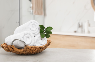 Photo of Rolled fresh towels and green leaves on grey table in bathroom. Space for text