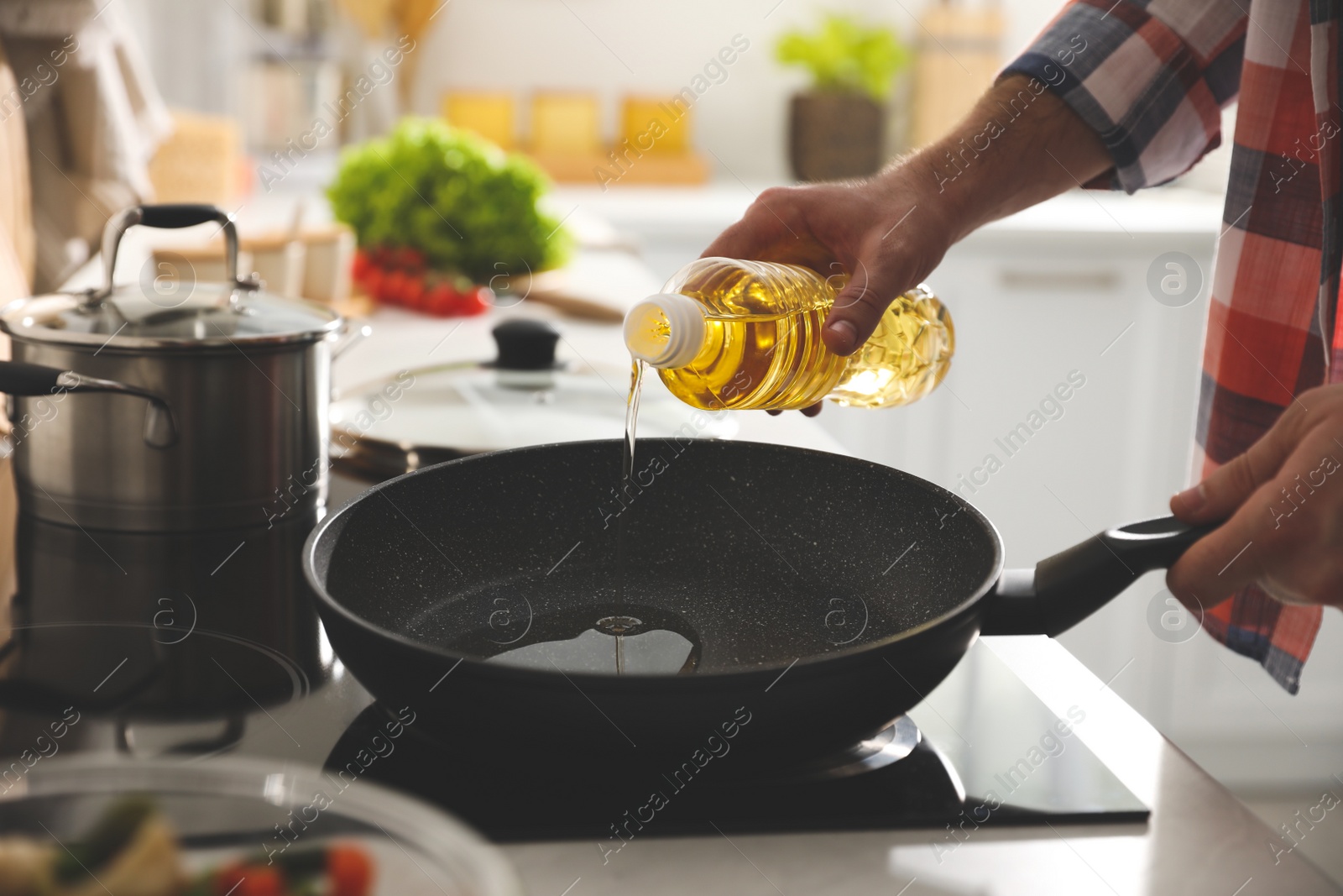 Photo of Man pouring cooking oil into frying pan in kitchen, closeup