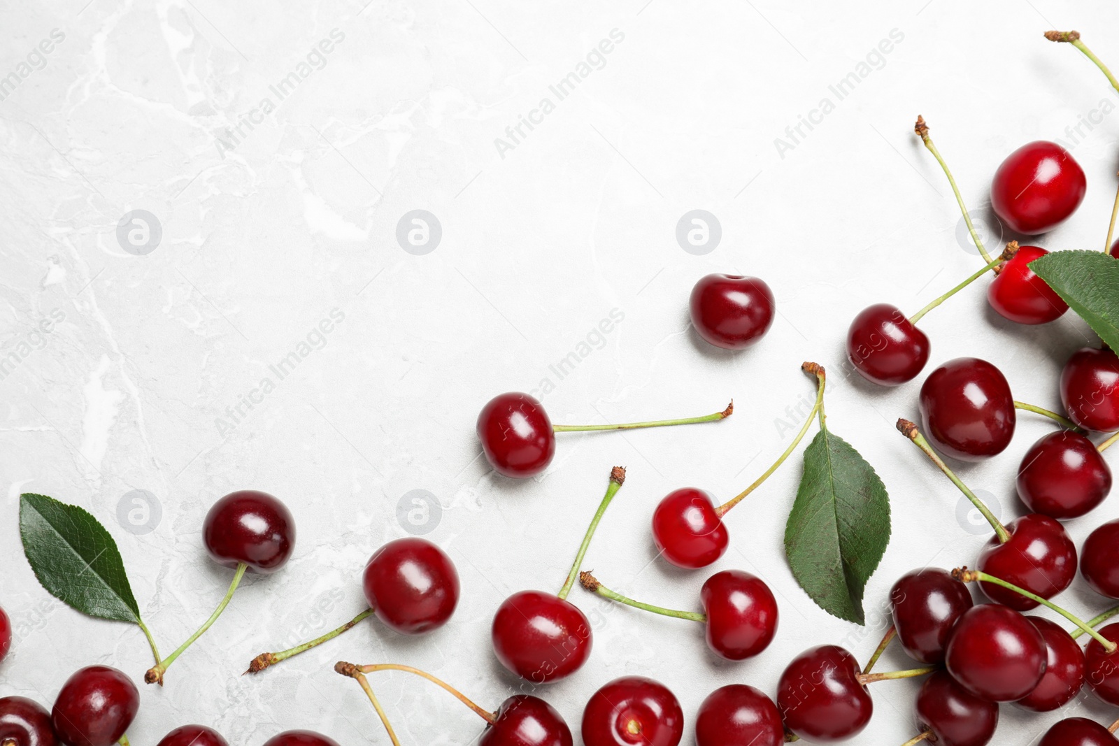 Photo of Sweet juicy cherries with leaves on grey marble table, flat lay. Space for text