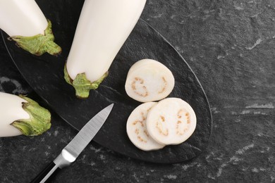 Board, raw white eggplants and knife on black textured table, flat lay. Space for text