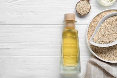 Glass bottle of sesame oil and seeds on white wooden table, flat lay. Space for text