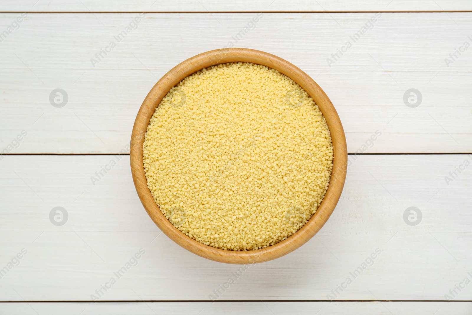 Photo of Bowl of raw couscous on white wooden table, top view