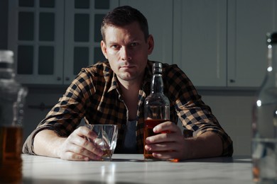 Addicted man with alcoholic drink at table in kitchen