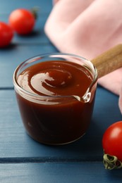 Photo of Tasty barbeque sauce and tomato on blue wooden table, closeup