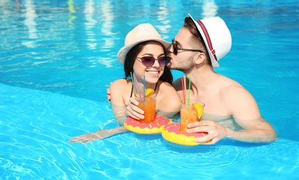 Young couple with refreshing cocktails in swimming pool on sunny day