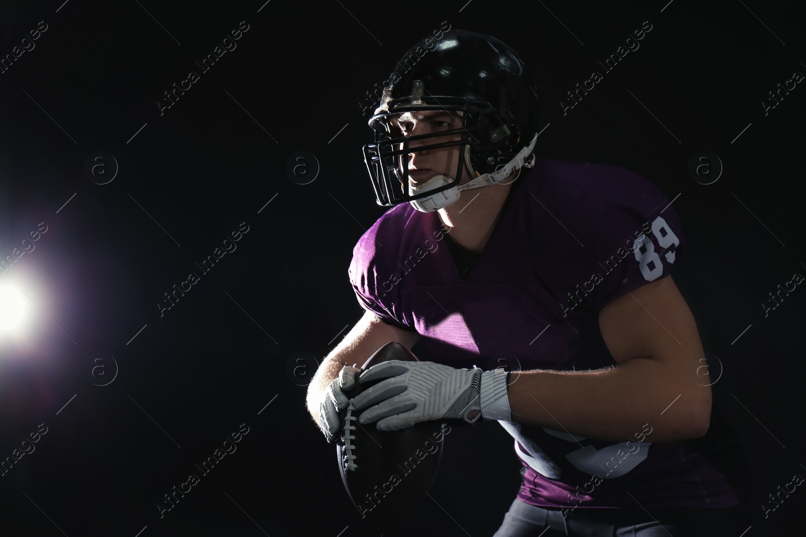 Photo of American football player with ball on dark background. Space for text