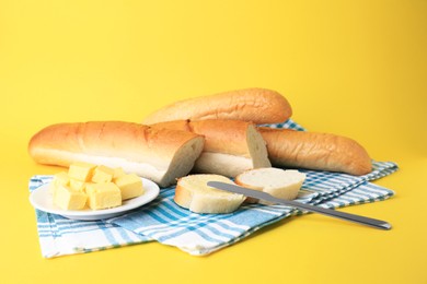 Photo of Whole and cut baguettes with fresh butter on yellow background