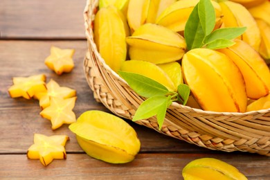 Cut and whole delicious ripe carambolas with wicker basket on wooden table, closeup