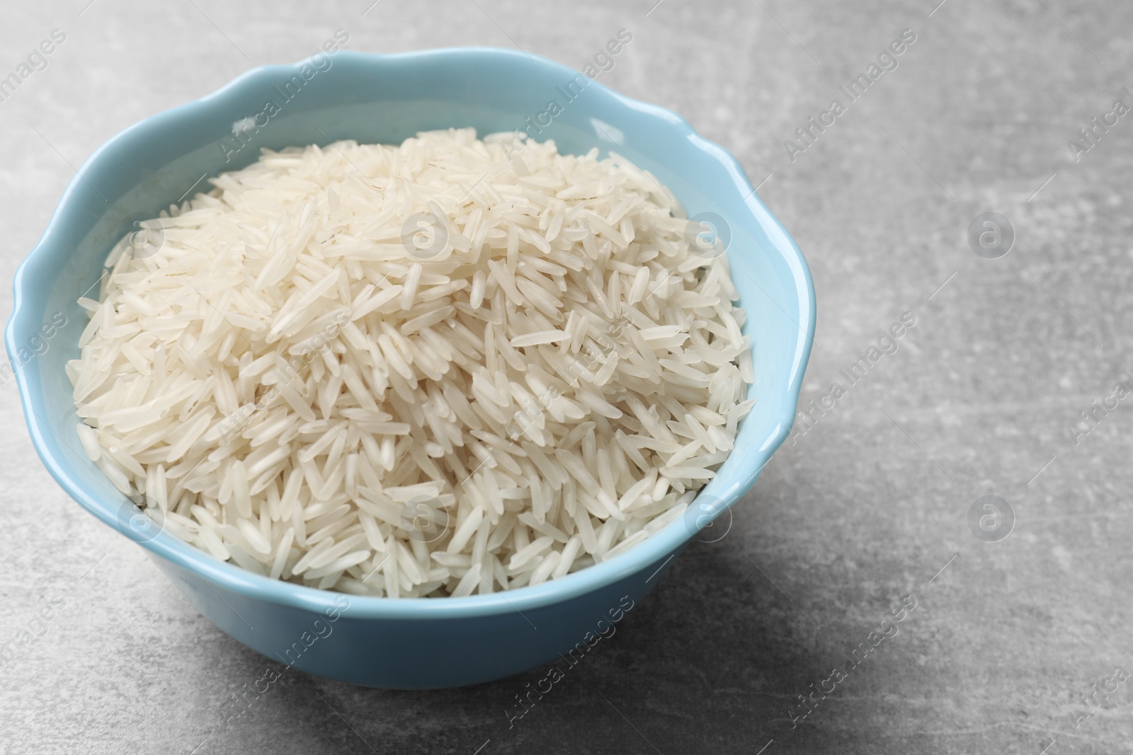 Photo of Raw basmati rice in bowl on grey table, closeup