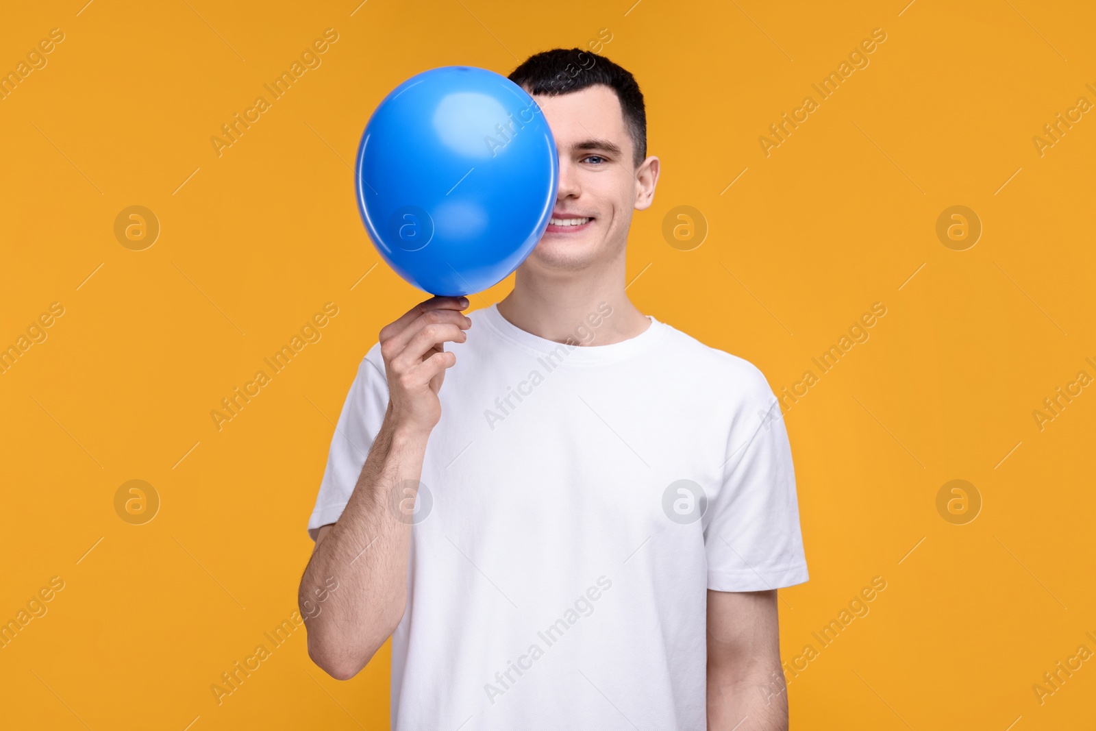 Photo of Happy young man with light blue balloon on yellow background