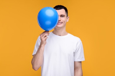 Photo of Happy young man with light blue balloon on yellow background
