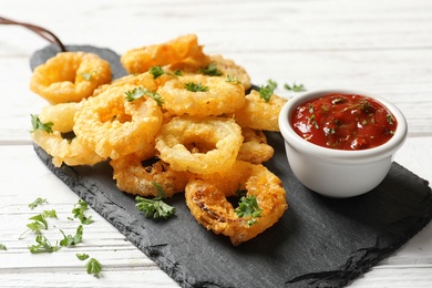 Homemade crunchy fried onion rings with tomato sauce on wooden table, closeup