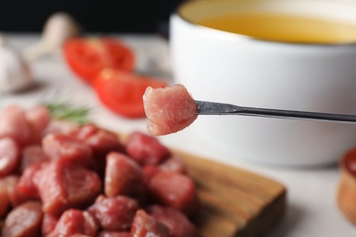 Photo of Fork with raw meat and blurred fondue pot on background, closeup