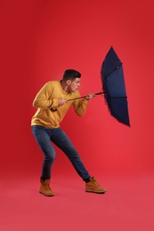 Emotional man with umbrella caught in gust of wind on red background