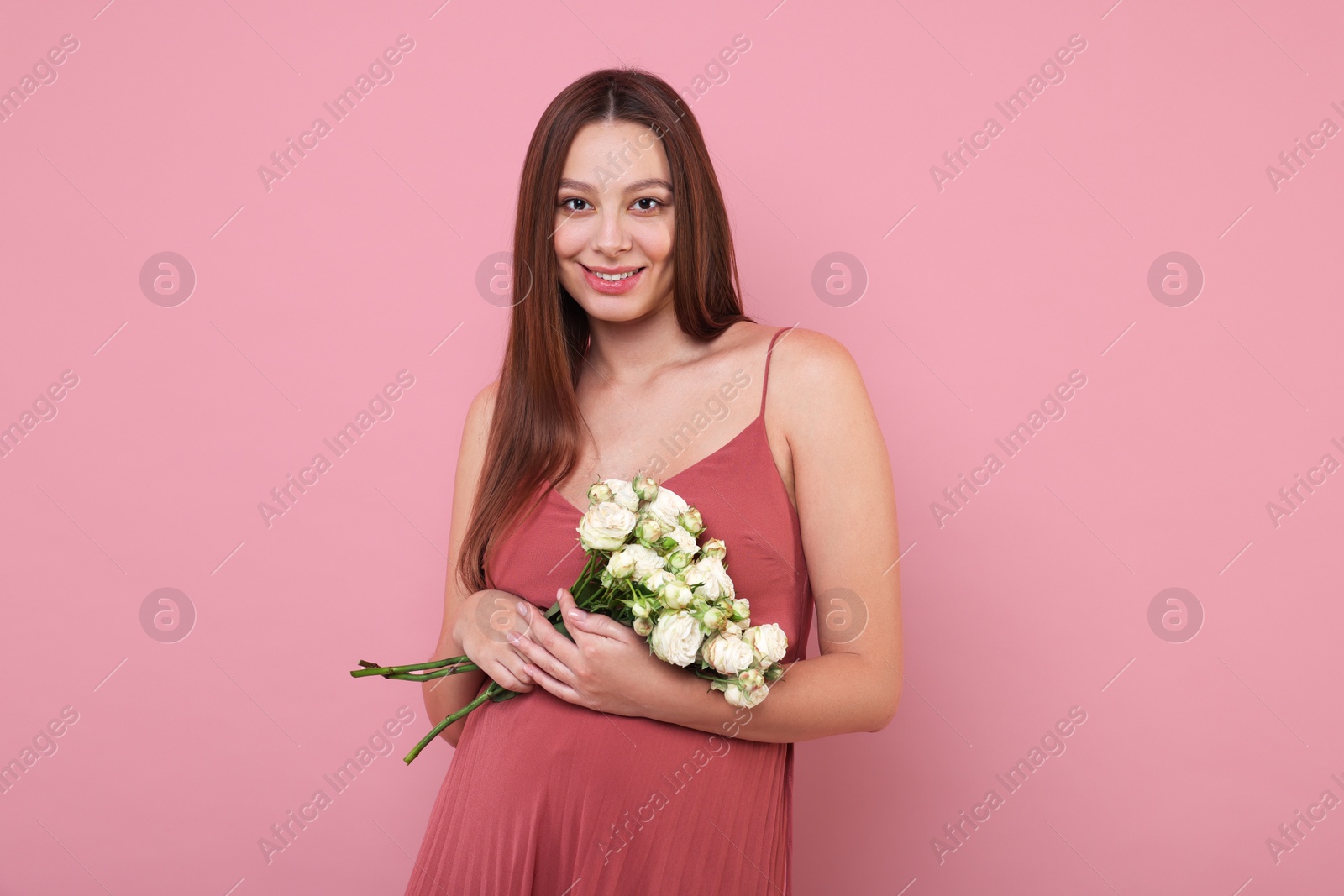 Photo of Beautiful pregnant woman in dress with bouquet of roses on pink background