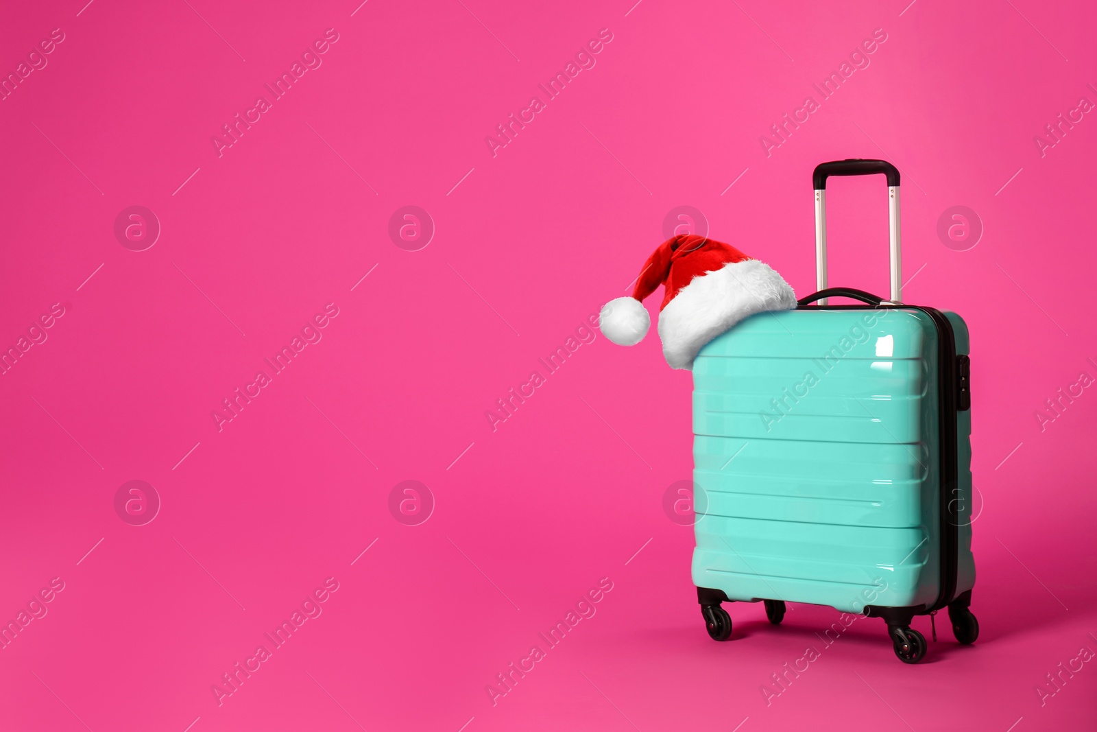 Image of Stylish suitcase with Santa Claus hat on pink background, space for text. Christmas vacation 