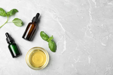 Flat lay composition with essential oils and basil on grey background. Space for text