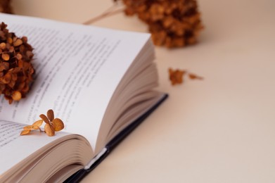 Photo of Dried hortensia flowers and book on beige table. Space for text