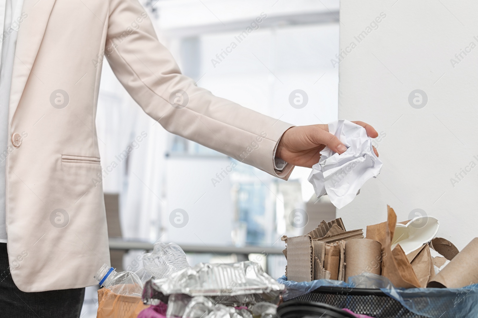 Photo of Woman putting crumpled paper into trash bin in office, closeup. Waste recycling