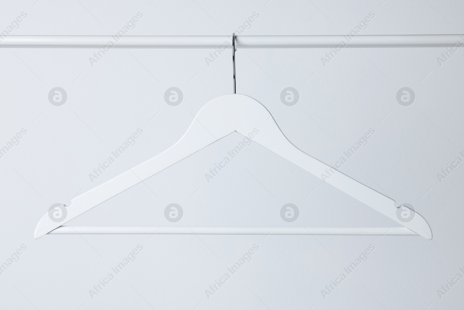 Photo of White clothes hanger on metal rail against light background