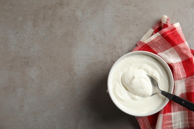 Photo of Bowl and spoon of fresh yogurt with napkin on grey background, flat lay. Space for text