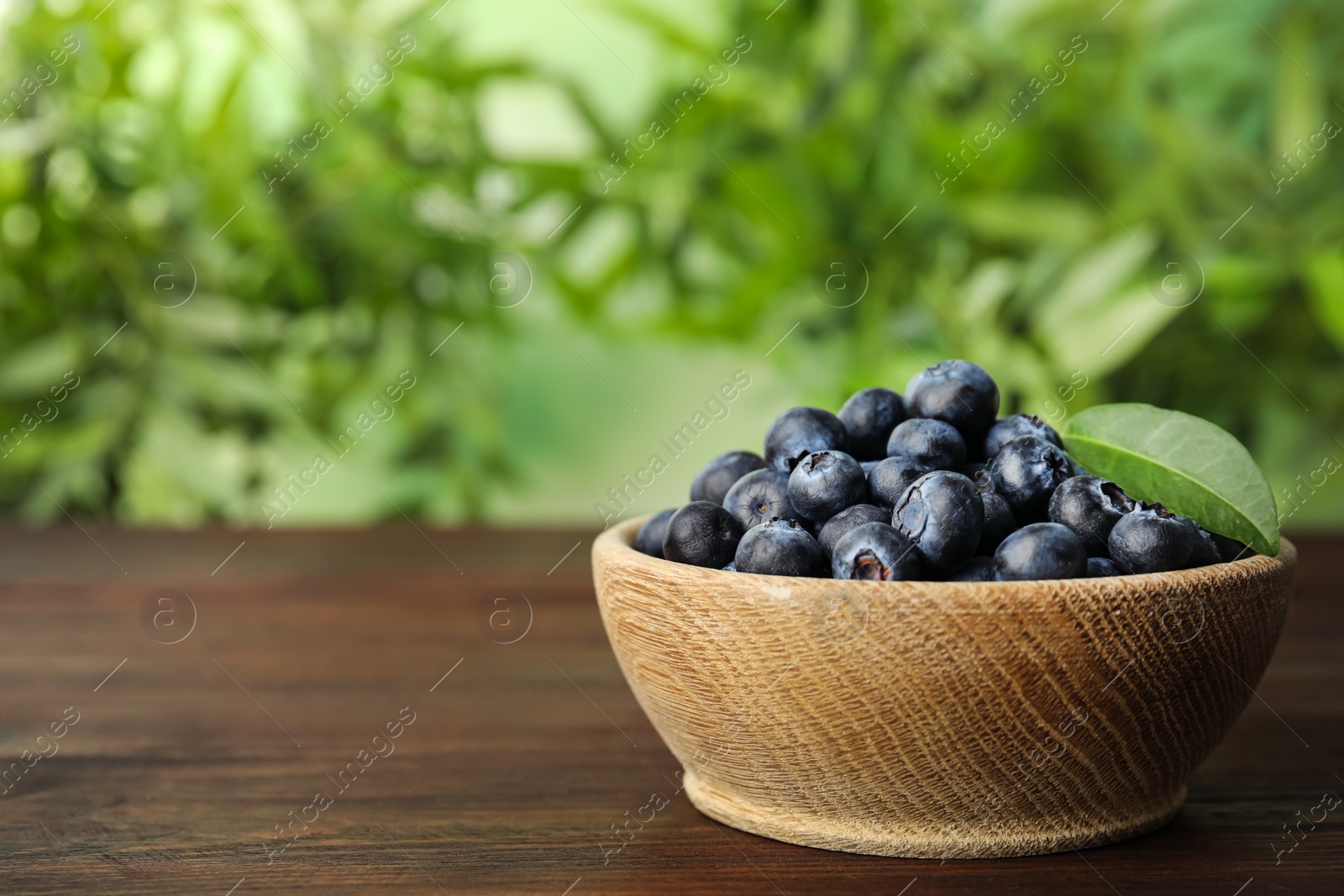 Photo of Tasty ripe blueberries in bowl on wooden table, space for text