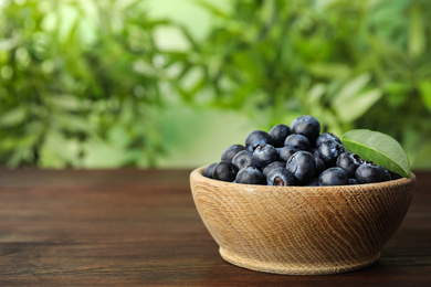 Photo of Tasty ripe blueberries in bowl on wooden table, space for text