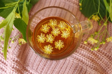 Photo of Glass cup of aromatic tea with linden blossoms on pink cloth, flat lay